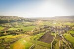 Das Foto zeigt Felder, Hügel, Sonne und ein kleines Dorf aus der Vogelperspektive