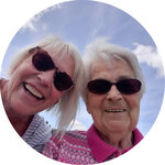 Zwei Frauen mit Sonnenbrille blicken lächelnd von oben in die Kamera. Im Hintergrund blauer Sommerhimmel.