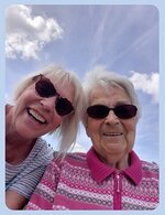 Zwei lächelnde Frauen mit Sonnenbrille schauen von oben in die Kamera. Darüber blauer Himmel mit ein paar Wolken und Sonnenstrahlen.